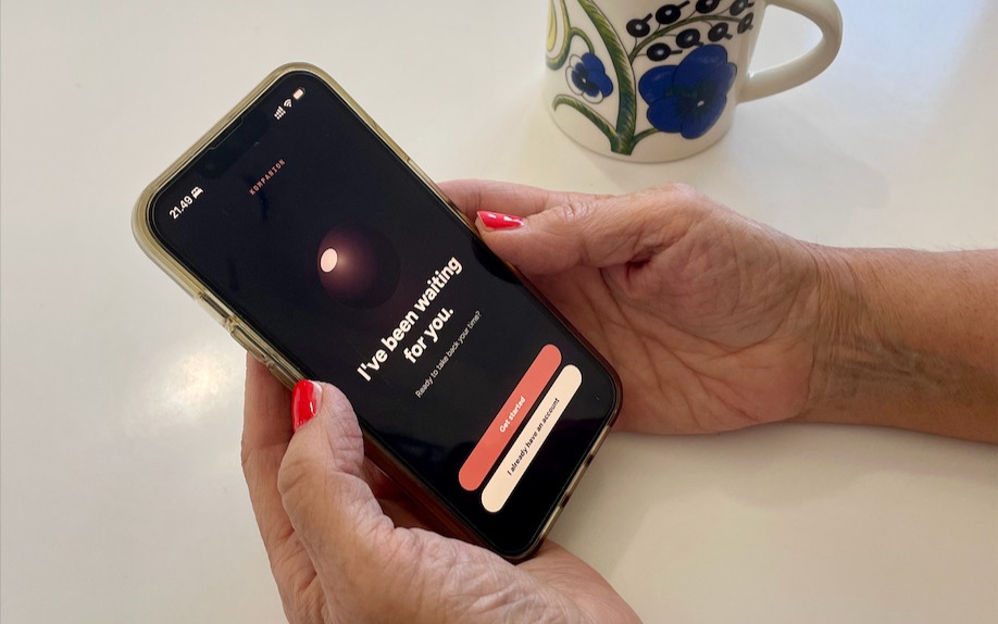 A user interview participant holding a phone with the onboarding prototype, over a white table beside a patterned mug. The app's dark welcome screen reads: I've been waiting for you. Ready to take back your time? Below are two buttons, Get started and I already have an account.